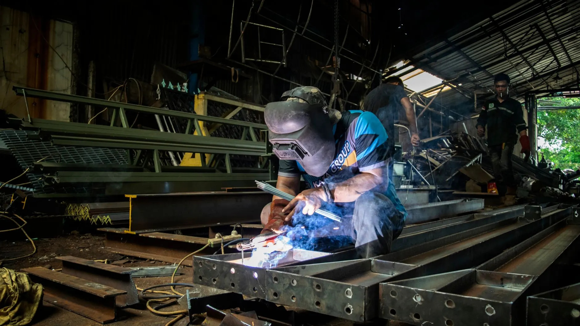 Custom-fabricated metal bracket clamped on a welding table with MIG torch and grinder nearby